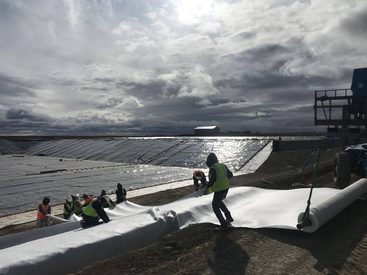 White geotextile unrolled from a spreader bar beside a lined pond